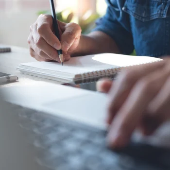 man writing on a pad while pressing a key on a keyboard